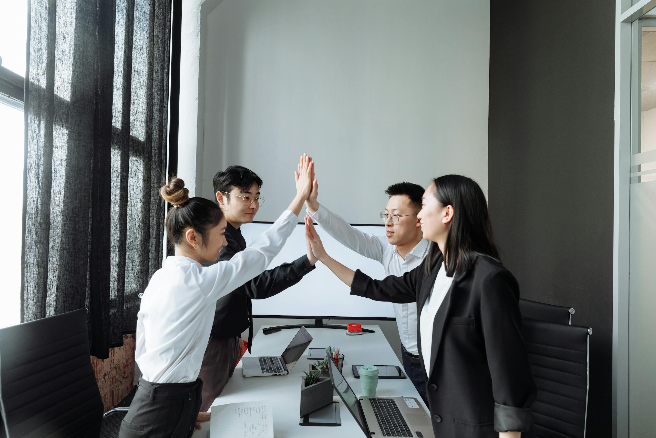 Four colleagues in a modern office high-fiving, celebrating teamwork and success.